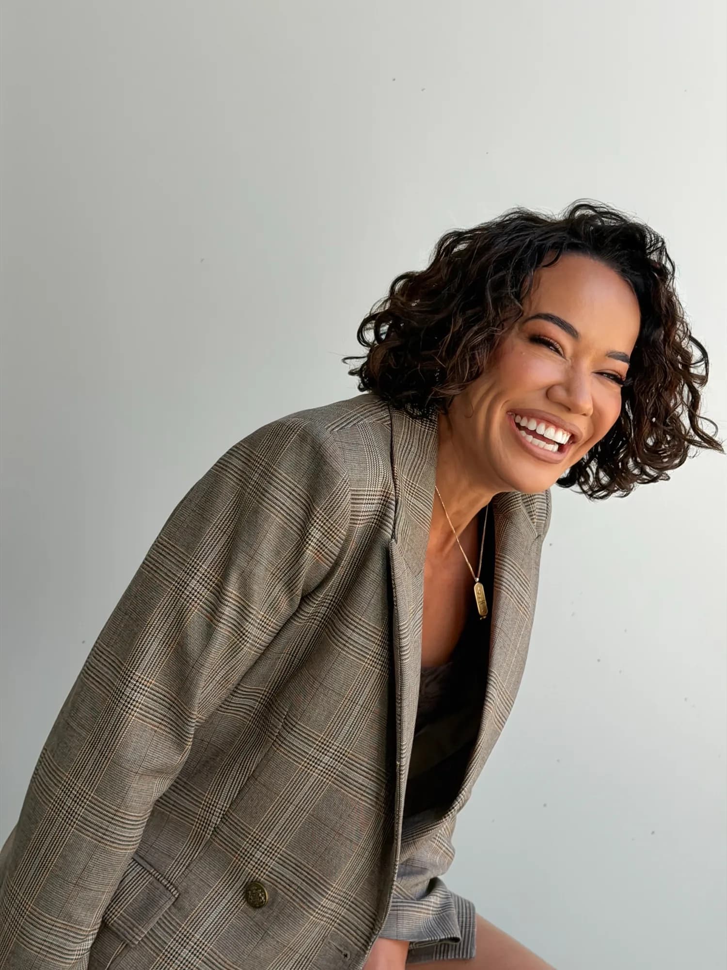 Delyse laughing warmly, leaning in, in a plaid blazer