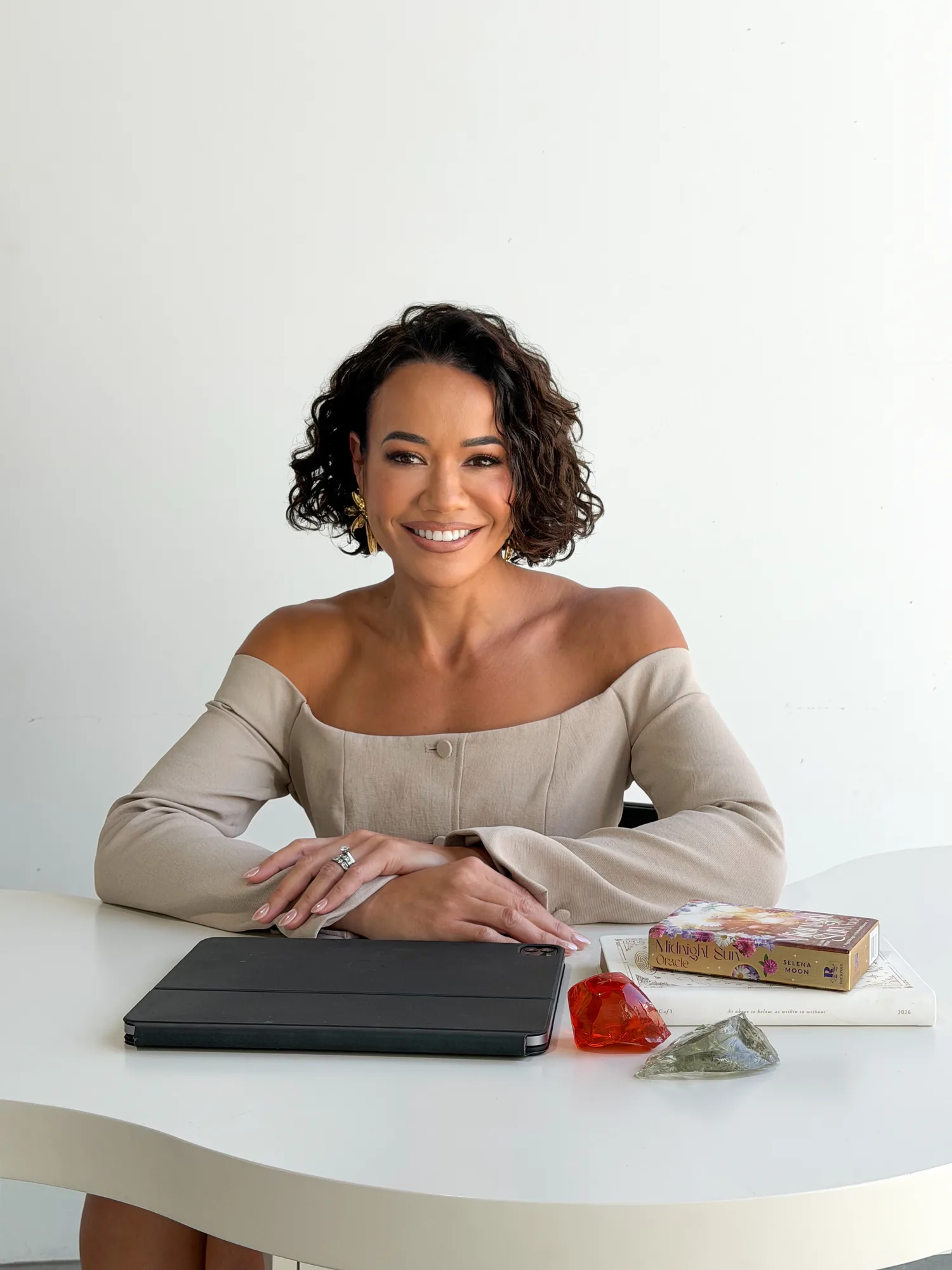 Delyse at her desk, smiling warmly, with books, an iPad and crystals